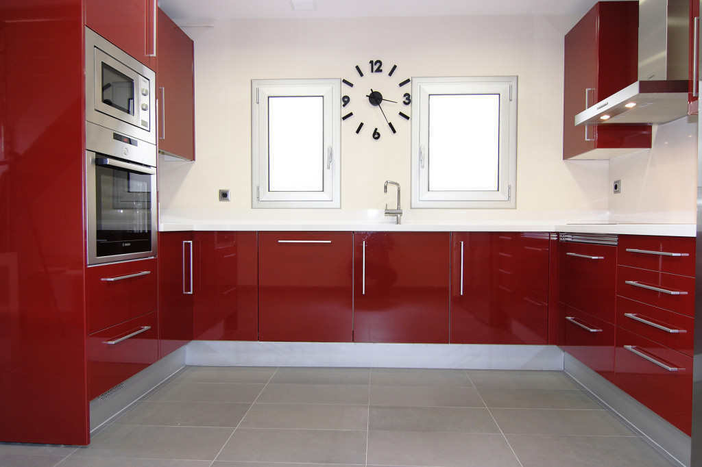 Moderní kuchyně červené barvy s bílou stěnou.